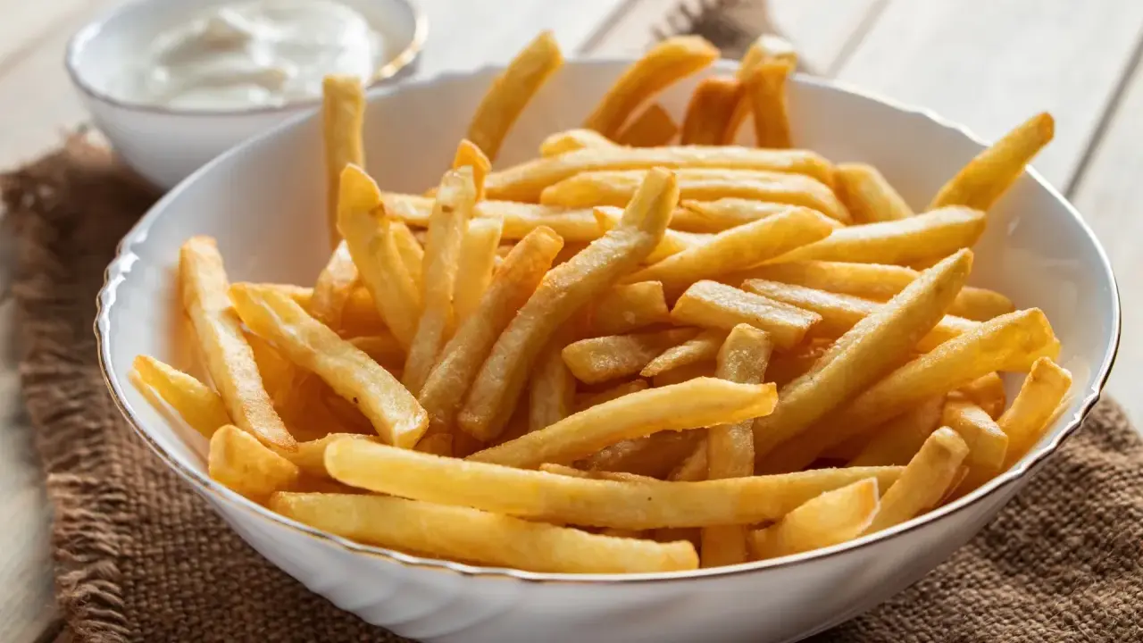 Chrupiące frytki z airfryer w białej misce, obok miseczka z sosem. Idealna przekąska na każdy dzień.