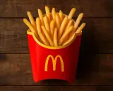 Złociste, chrupiące frytki McDonald's w czerwonym opakowaniu z logo, gotowe do schrupania na drewnianym tle.