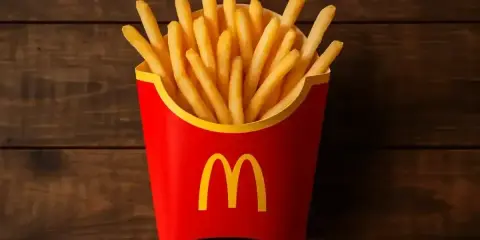 Złociste, chrupiące frytki McDonald's w czerwonym opakowaniu z logo, gotowe do schrupania na drewnianym tle.