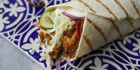 Pyszny kebab w picie z soczystym mięsem, chrupiącą kapustą, pomidorem, ogórkiem i czerwoną cebulą, podany na ozdobnym talerzu.
