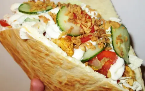 Pyszna bułka kebab z kurczakiem, warzywami i chrupiącą cebulką.