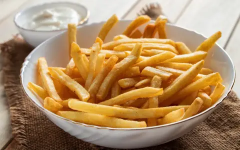 Chrupiące frytki z airfryer w białej misce, obok miseczka z sosem. Idealna przekąska na każdy dzień.