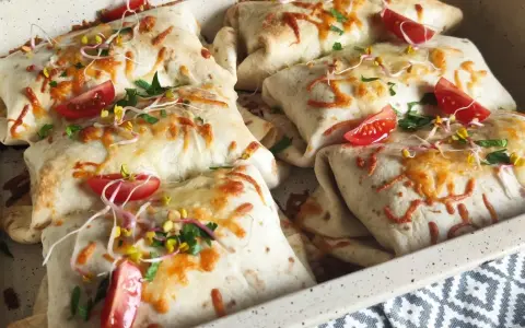 Tortilla z mięsem mielonym i serem, zapieczona z pomidorkami i kiełkami. Pyszne danie gotowe do podania.