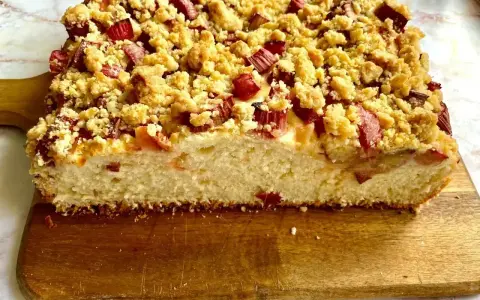 Puszyste ciasto drożdżowe z rabarbarem i kruszonką, pokrojone na desce.