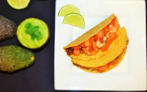 Pyszne meksykańskie tacos przepis na talerzu, z awokado i limonką w tle. Idealne na szybki obiad!