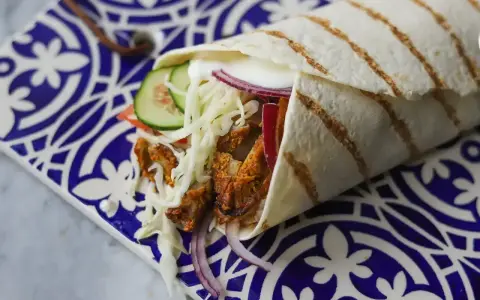 Pyszny kebab w picie z soczystym mięsem, chrupiącą kapustą, pomidorem, ogórkiem i czerwoną cebulą, podany na ozdobnym talerzu.