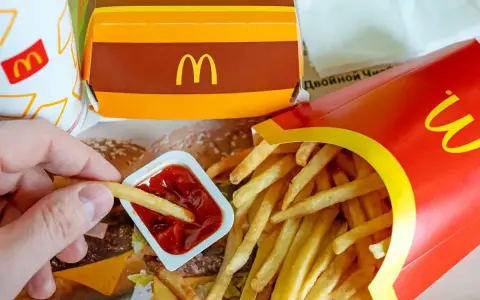 Ręka zanurza frytkę w keczupie. Obok pudełko z frytkami i burgerem. McDouble kcal to smak, który znasz.