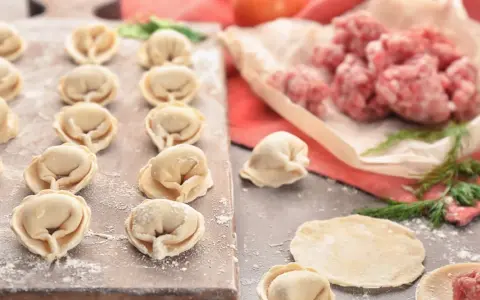 Gotowe do lepienia pierogi z mięsem mielonym surowym. Na desce ułożone pierożki, obok surowe mięso i ciasto.