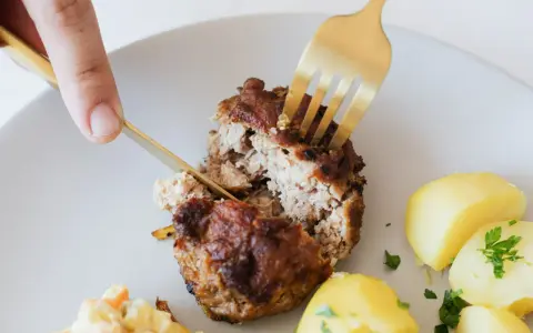 Kotlety mielone przepis babci: soczysty kotlet rozkrajany widelcem, obok ziemniaczki i surówka.