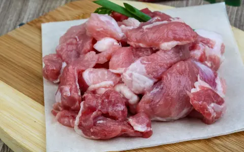 Surowe, pokrojone w kostkę mięso wieprzowe, idealne na gulasz. W tle czosnek i papryczki chili.