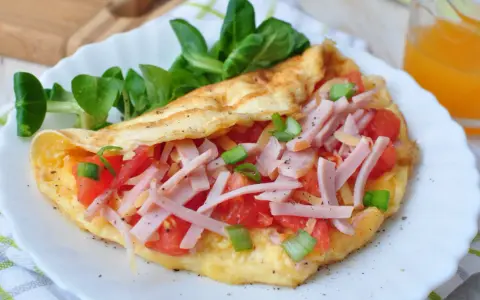 Pyszny omlet bez mąki z szynką, pomidorami i szczypiorkiem, podany z sałatką. Idealny na szybkie śniadanie.