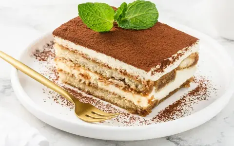 Pyszny kawałek tiramisu z mascarpone, posypany kakao i udekorowany miętą. Idealny na deser.