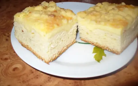Dwa kawałki puszystego ciasta drożdżowego z serem, posypane kruszonką, na białym talerzu.