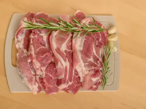 Surowe kawałki wieprzowiny z rozmarynem i czosnkiem, idealne jako jakie mięso do bigosu.