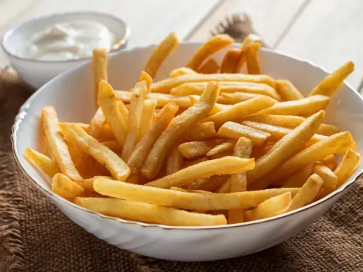 Chrupiące frytki z airfryer w białej misce, obok miseczka z sosem. Idealna przekąska na każdy dzień.