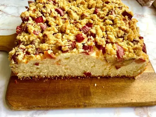 Puszyste ciasto drożdżowe z rabarbarem i kruszonką, pokrojone na desce.