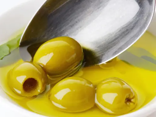 Kilka zielonych oliwek w złocistej oliwie, łyżka zanurzona w płynie. Oliwa z oliwek kcal - zdrowie i smak.
