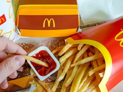Ręka zanurza frytkę w keczupie. Obok pudełko z frytkami i burgerem. McDouble kcal to smak, który znasz.