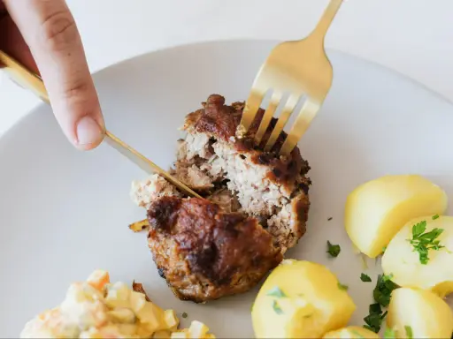 Kotlety mielone przepis babci: soczysty kotlet rozkrajany widelcem, obok ziemniaczki i surówka.