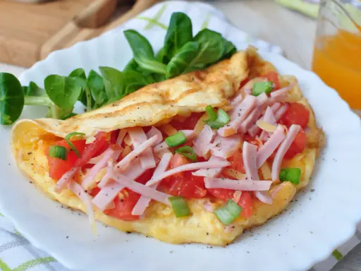 Pyszny omlet bez mąki z szynką, pomidorami i szczypiorkiem, podany z sałatką. Idealny na szybkie śniadanie.