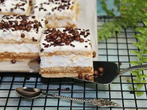 Pyszne ciasto 3 bit bez pieczenia, z kremem i czekoladowymi kuleczkami, prezentuje się apetycznie na paterze.