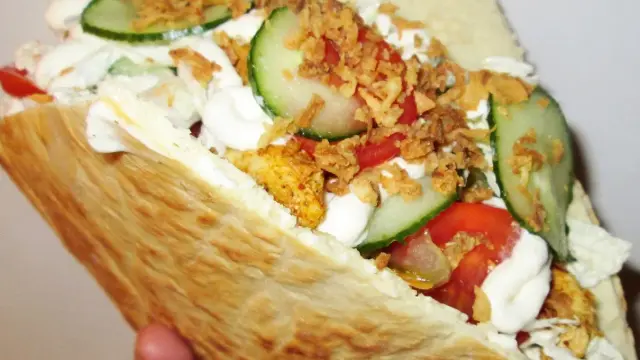 Pyszna bułka kebab z kurczakiem, warzywami i chrupiącą cebulką.