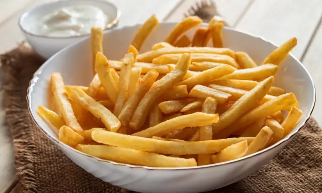 Chrupiące frytki z airfryer w białej misce, obok miseczka z sosem. Idealna przekąska na każdy dzień.