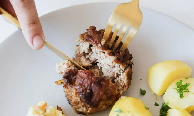 Kotlety mielone przepis babci: soczysty kotlet rozkrajany widelcem, obok ziemniaczki i surówka.