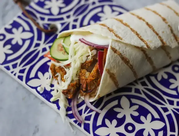 Pyszny kebab w picie z soczystym mięsem, chrupiącą kapustą, pomidorem, ogórkiem i czerwoną cebulą, podany na ozdobnym talerzu.